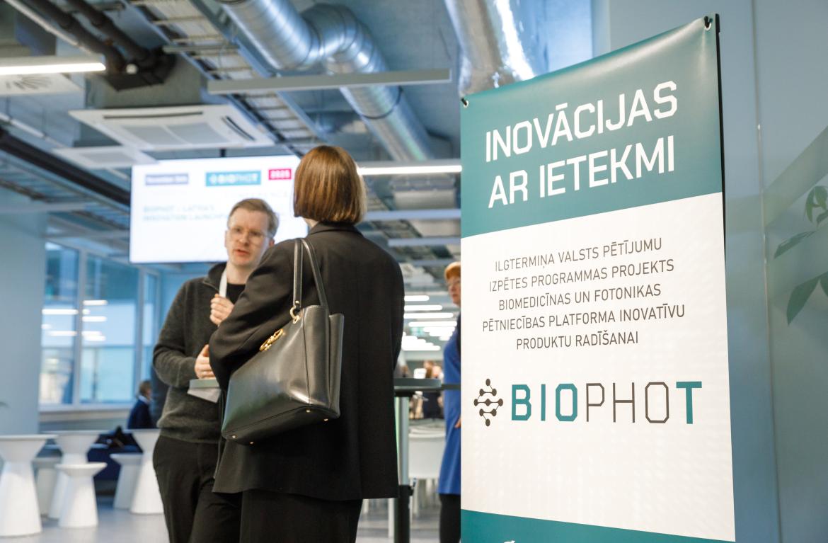 BioPhot plakāts kuram blakus runājas divas sievietes